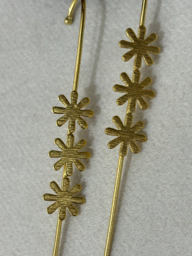 A pair of gold wire earrings featuring three textured starburst or asterisk-shaped studs on each earring, displayed on a light gray textured background.